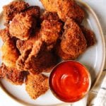 Homemade chicken nuggets on a white plate with ketchup